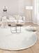 Beige Sofa mit Kissen und Decke vor runden Tischen auf weißem Teppich im hellen Wohnzimmer.
