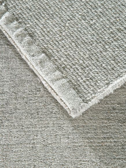 Zwei übereinanderliegende graue Teppiche mit unterschiedlicher Textur auf hellem Untergrund.
