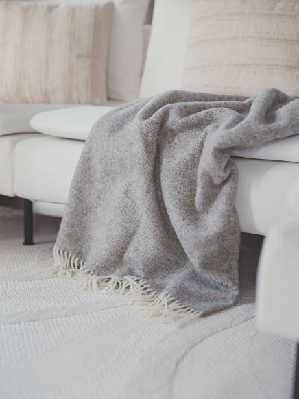 Graue Decke liegt locker auf weißem Sofa in hell eingerichtetem Wohnzimmer mit Teppich.