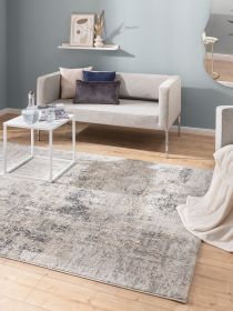 Beiges Sofa mit Kissen steht vor blauer Wand, weißer Tisch mit Karaffe, moderner Teppich liegt auf Holzfußboden.