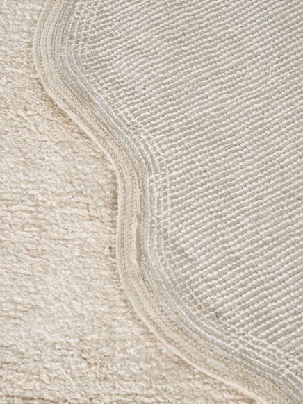Naht an zwei Teppichen, ein Teppich gewellt, beide in hellen Beige- und Grautönen auf hellem Boden.