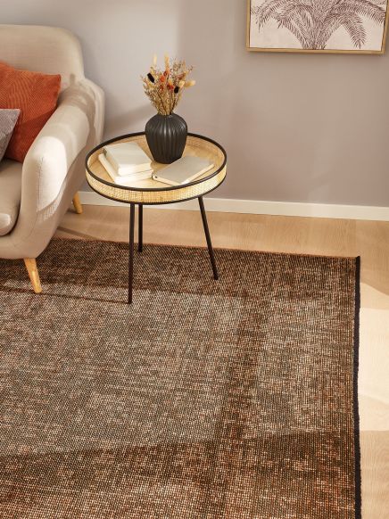 Beistelltisch mit Vase und Büchern neben beige Sofa auf braunem Teppich im Wohnzimmer.