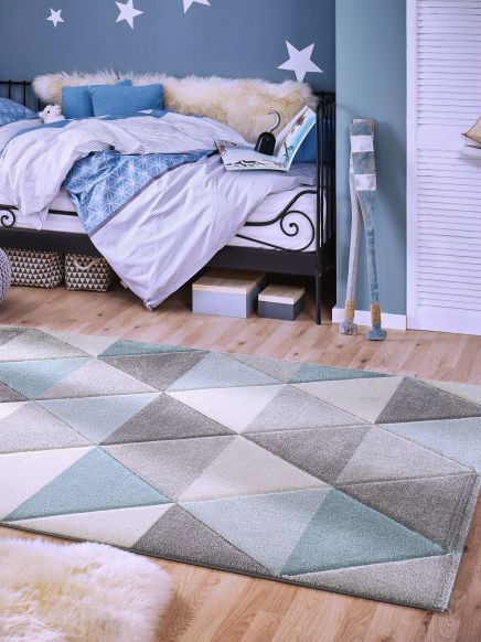 Teppich liegt auf Holzboden vor blauem Bett mit Decke und Kissen, Wand mit weißen Sternen.