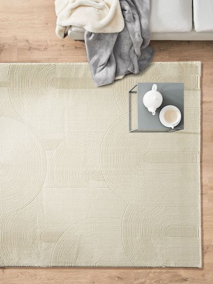 Becher und Teekanne stehen auf kleinem grauen Tisch auf gemustertem Teppich neben grauer Couch mit Decken.