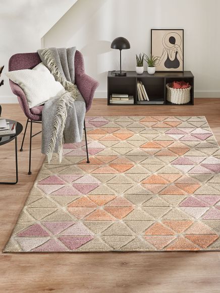 Stuhl mit Decke und Kissen steht auf Teppich mit geometrischem Muster in modernem Raum.