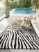 Zebra gemusterter Teppich liegt auf Boden, zwei Beistelltische stehen davor, Sofa und Pool im Hintergrund.