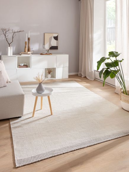 Kleiner runder Tisch mit Vase steht auf hellem Teppich in modern eingerichteten Wohnzimmer.