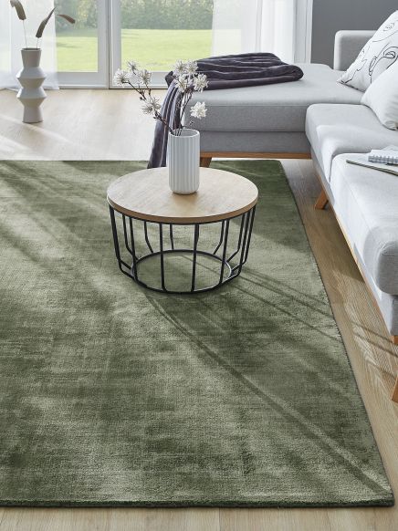 Runder Couchtisch mit Vase und weißen Blumen steht auf grünem Teppich neben grauem Sofa im Wohnzimmer.