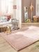 Kuscheliger rosa Teppich auf Holzfußboden neben Sofa mit Kissen und Decke rechts Spiegel und Schaufensterpuppe im Raum
