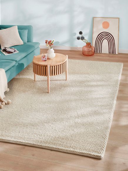 Teppich liegt auf Holzboden Sofa mit Kissen und Tisch mit Vase im Raum weiße Wand mit Kunstwerk im Hintergrund