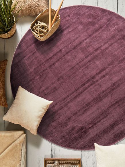 Runder violetter Teppich auf Holzboden umgeben von Kissen Pflanze und Korb mit Stricknadeln