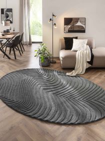 Ovaler grauer Teppich mit gewelltem Muster auf Holzboden vor Sofa und Stehlampe im Wohnzimmer.