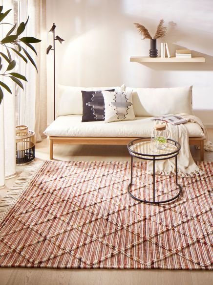 Sofa mit Kissen und Decke, Beistelltisch mit Karaffe und Gläsern, Teppich im hellen Wohnzimmer.