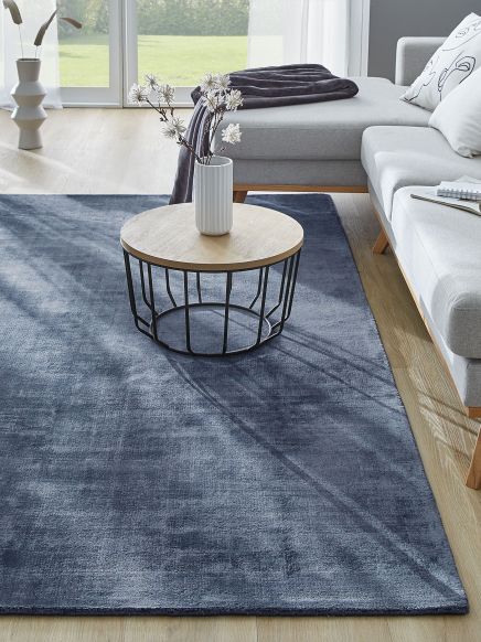 Moderner runder Couchtisch mit Vase auf blauem Teppich vor grauem Sofa im Wohnzimmer.