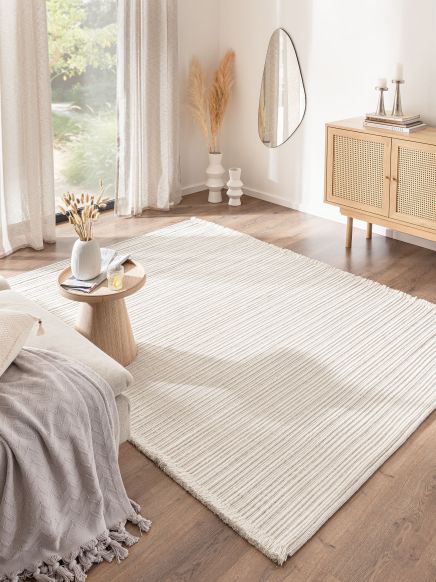 Heller Teppich liegt auf Holzboden, daneben ein Beistelltisch mit Vase, hellem Sofa und Sideboard.