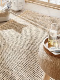 Naturfaser-Teppich liegt auf Holzboden neben Tisch mit Karaffe und Glas in sonnigem Raum