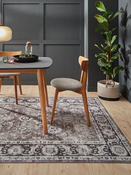 Stuhl steht neben Tisch mit Gläsern auf dekorativem Teppich in modernem Esszimmer.
