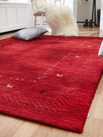 Roter Teppich auf Holzboden mit Kissen und Fellhocker im Wohnraum links Fenster im Hintergrund.
