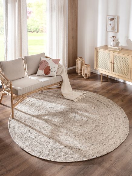 Runder Teppich auf Holzboden neben Sofa mit Kissen und Decke vor Fenster in modernem Wohnzimmer