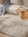 Beiger Teppich liegt unter einem Sofa mit Decke und einem kleinen Holztisch mit Vase, Glas und Magazin.