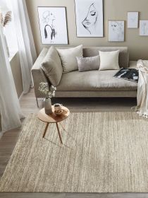 Beiger Teppich liegt unter kleinem Holztisch mit Vase, Tasse und Schale vor Sofa mit Kissen im Wohnzimmer.