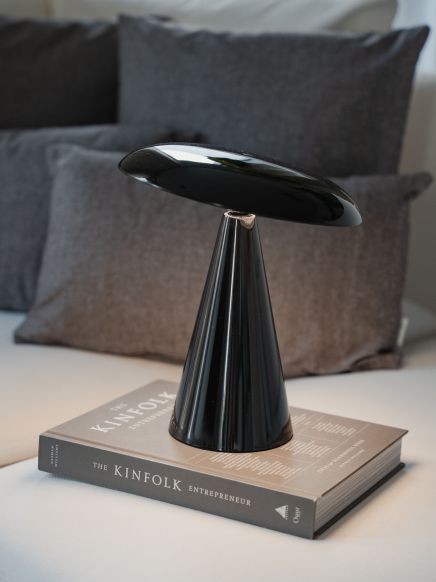 Schwarze Lampe steht auf Buch mit Titel "The Kinfolk Entrepreneur" vor grauen Kissen.