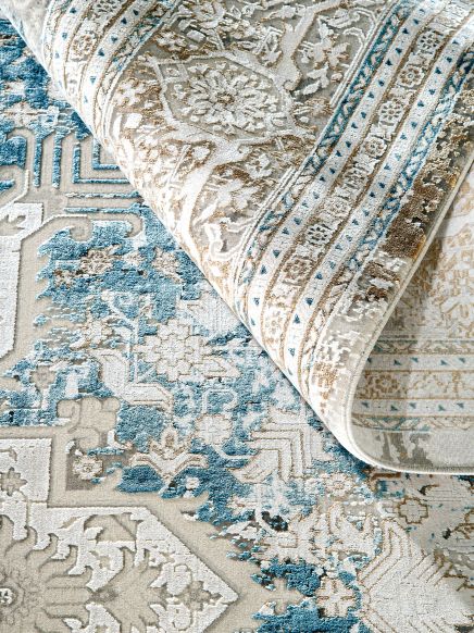 Teppich liegt auf anderem Teppich, zeigt florales Muster in Beige, Blau und Braun in Nahaufnahme.