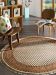 Runder gemusterter Teppich liegt auf Holzboden, zwei Holzstühle daneben mit Kissen und Buch.