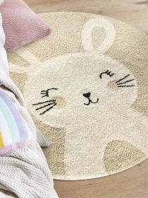 Runder Teppich mit Hasenmotiv liegt auf Holzboden neben buntem und rosafarbenem Kissen.