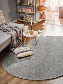 Runder grauer Teppich auf Holzboden unter rundem Tisch mit Deko in modernem Wohnzimmer mit Sofa und Regal