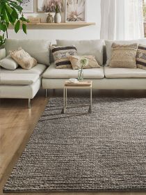Beige Sofa mit gemusterten Kissen, kleiner Beistelltisch mit Tasse und Blume vor einem großen Teppich.