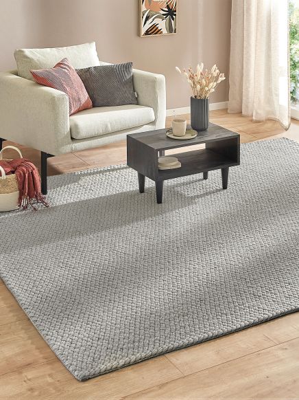 Beiger Sessel steht neben einem schwarzen Couchtisch auf grauem Teppich in hellem Zimmer.